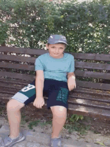 a young boy is sitting on a wooden bench wearing a blue shirt and shorts with the number 8 on them