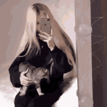 a girl is taking a selfie with her phone while holding a cat .