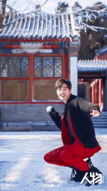 a man in red pants is squatting in the snow in front of a building with chinese writing on it