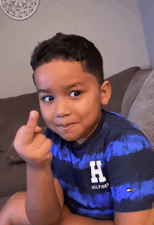 a young boy wearing a blue striped shirt with the letter h on it giving the middle finger