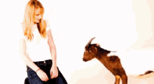 a woman is kneeling down next to a small goat that is standing on its hind legs .