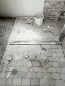 a bucket of concrete sits on a brick floor next to a drain