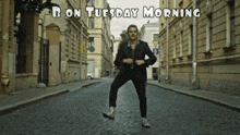 a man dancing on a cobblestone street with the words " b on tuesday morning " below him