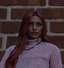 a woman with red hair wearing a pink sweater and sunglasses