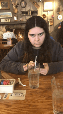 a girl is sitting at a table with a glass of water and a straw in her mouth