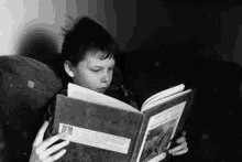 a boy is reading a book while sitting on a couch .