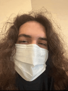 a man with long curly hair wears a white face mask