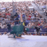 a man in a green shirt is doing a trick in front of a crowd with a paris sign behind him