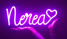 a person is holding a purple neon sign that says nerea with a heart .