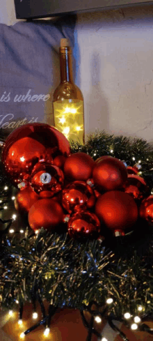 a bottle of wine sits next to a bunch of red ornaments