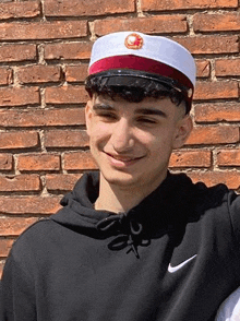 a young man wearing a graduation cap and a black nike hoodie is standing in front of a brick wall .