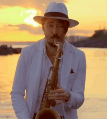 a man in a white hat is playing a saxophone on the beach