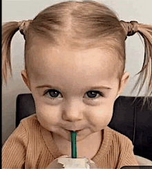 a little girl with pigtails drinking through a straw .