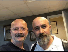 two bald men with beards and mustaches are posing for a picture together .