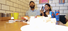 a man and woman sitting at a table with pepsi cans