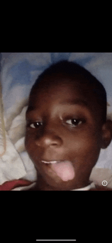 a young boy is sticking his tongue out while laying down on a bed .