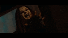 a woman with a scary face is standing in a dark room with her hands out .