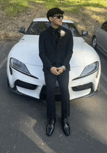 a man in a suit and sunglasses is standing in front of a white sports car .