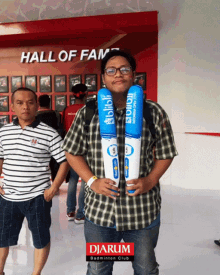 a man in a plaid shirt is holding a pair of blue and white balloons with the word hall of fame behind him