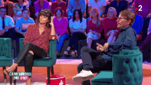 a woman sits in a chair next to a man in front of a crowd with the number 2 visible