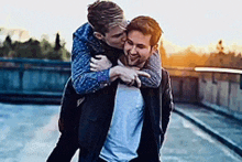 a man is carrying another man on his back while kissing him on the cheek .