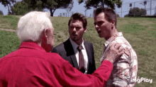 three men are standing in a grassy field and one of them is wearing a red shirt and tie .