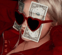 a woman wearing heart shaped sunglasses is holding a dollar bill over her eyes