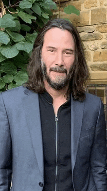 a man with long hair and a beard is standing in front of a stone wall .