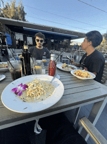 two men sit at a table with plates of food and a ketchup bottle