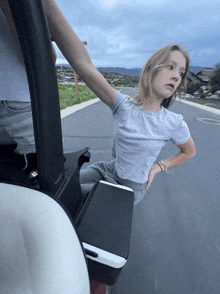 a girl in a grey t-shirt is standing in a golf cart