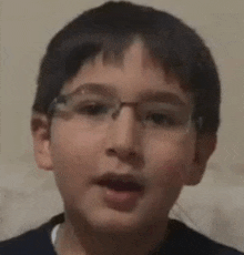 a young boy wearing glasses is making a funny face and looking at the camera .