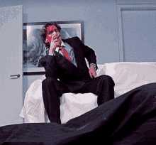 a man in a suit and tie is sitting on a couch with blood on his face smoking a cigarette