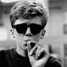 a man wearing sunglasses is smoking a cigarette in a black and white photo