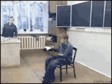 a boy is sitting in a chair in a classroom reading a book while a teacher stands behind him .