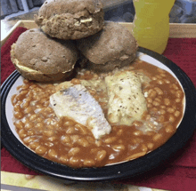 a plate of baked beans with fish and biscuits next to a bottle of orange juice