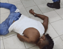 a man in a white tank top and blue jeans is laying on the floor