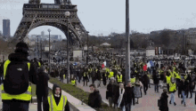 a man wearing a north face backpack is taking a picture of a crowd of people walking in front of the eiffel tower