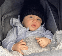 a baby wearing a black hat and a grey jacket is sitting in a car seat