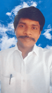 a man with a mustache wearing ear buds looks at the camera with a blue sky in the background