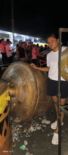 a woman is standing in front of a large drum that says poco x4 gt on the bottom right