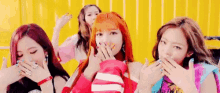 a group of girls are covering their mouths with their hands in front of a yellow background .