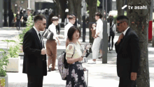 a man in a suit stands next to a woman in a floral skirt and a sign that says tv asahi