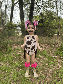 a little girl wearing a cow print outfit and cowboy boots smiles for the camera