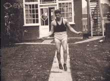 a black and white photo of a man jumping a rope in front of a house with the word eye on the bottom right