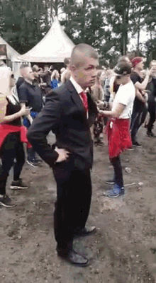 a man in a suit and tie is standing in front of a crowd of people at a festival .