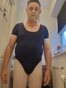 a man wearing a black leotard stands in a bathroom