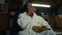 a person in a bathrobe is eating popcorn with the fallout logo in the background