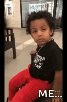 a young boy wearing a black shirt and red pants is sitting on a bench in a waiting room .