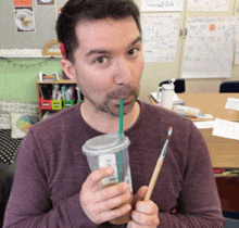 a man in a purple shirt drinks from a plastic cup with a straw