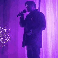 a man singing into a microphone in front of a purple background